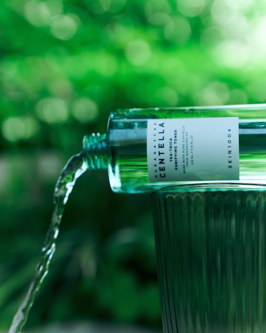 Attīrošs SKIN1004 Madagascar Centella Tea-Trica pūderojošs toniks, 210ml, uz galda ar sastāvdaļām un iepakojumu.