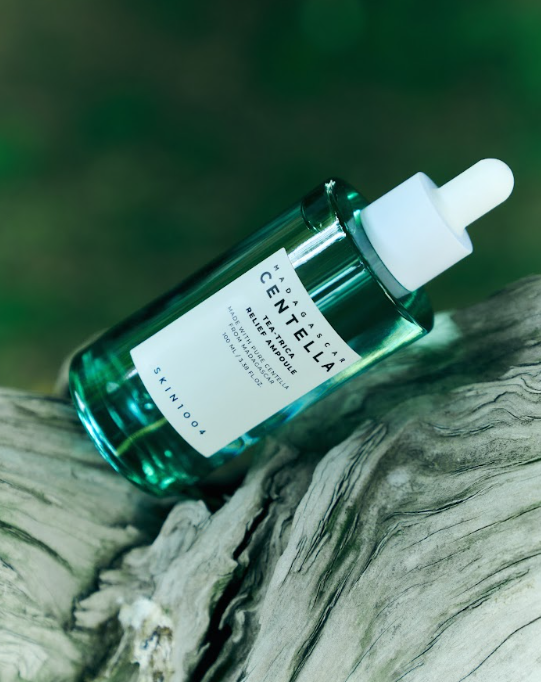 YABUKO SKIN1004 Madagaskaras Centella Tea-Trica nomierinoša ampula, 100 ml, uz rokām ar zaļām augu sastāvdaļām.